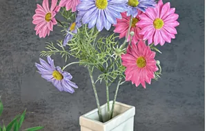 Detailopname van roze en paarse kunstmatige cosmosbloemen met groene bladeren in witte vaas