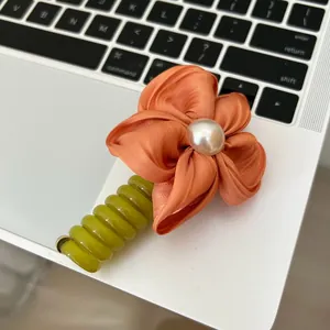 Detail of a handmade fabric flower hair tie with an orange petal and a central pearl accent