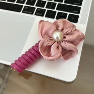 Detail of pink satin flower hair tie with pearl center on a laptop keyboard