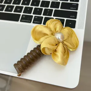 Detailed macro view of yellow satin flower hair clip with pearl on laptop keyboard
