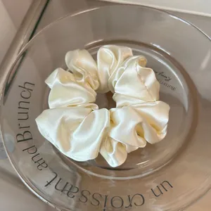 Close-up of a cream satin scrunchie with glossy texture on a glass display plate