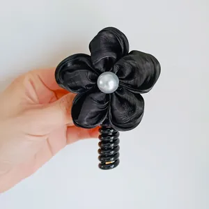 Close-up of black satin flower hair tie with pearl center and spiral cord strap