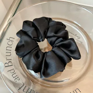 Close-up of elegant black satin scrunchie featuring smooth silk texture and soft cloud pleats