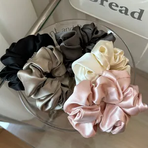 Five assorted glossy satin hair scrunchies in a glass bowl for elegant hairstyling
