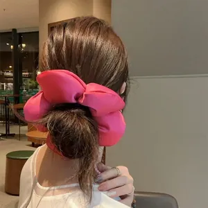 Détail d'un chouchou volumineux en tissu rose porté en chignon haut dans un café cosy