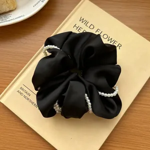 Detail of a large black satin scrunchie with layered pearl beads on a book surface