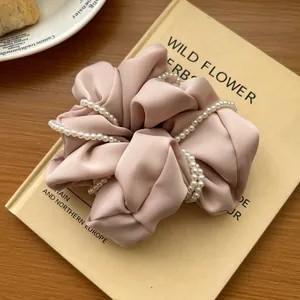 Detail view of pink satin scrunchie with double faux pearl beads on a book surface