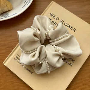 Close-up of a creamy white faux leather scrunchie with wrapped faux pearls texture
