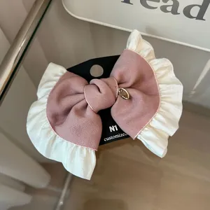 Detail of pink bow hair clip with white ruffle edges and golden pendant on black card
