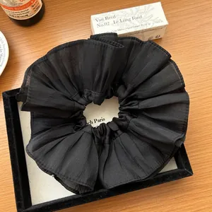 Close-up of large black pleated chiffon scrunchie on a premium wooden display surface