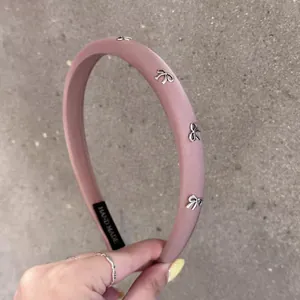 Détail du serre-tête rose rembourré avec nœuds métalliques et étiquette logo