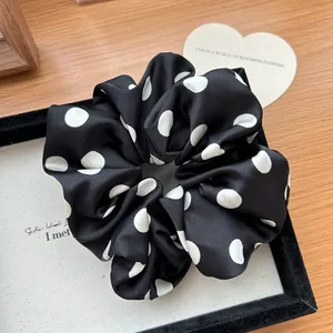 Dettaglio dell'elastico per capelli in raso a pois bianchi e neri su un vassoio