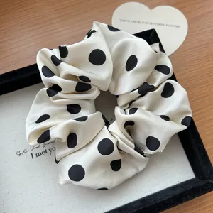 Primo piano di un elastico scrunchie in raso a pois neri su tessuto color avorio