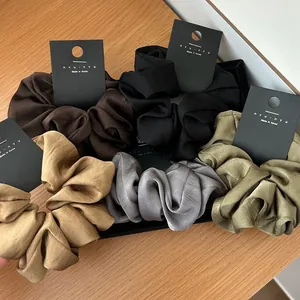 Five assorted vintage satin scrunchies in Morandi tones on a warm wooden surface