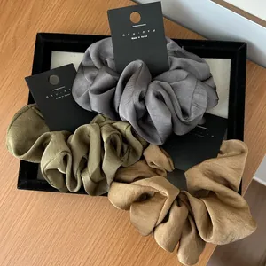 Close-up of three satin scrunchies in grey, green and gold on a jewelry tray
