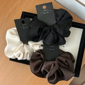 Detailed view of silk satin scrunchies in black, cream, and brown on a white tray