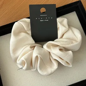 Macro detail of cream textured scrunchie with nyunyu tag on a beige display tray