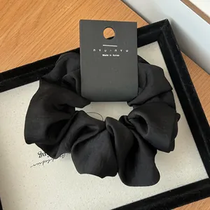 Close-up of black satin scrunchie on a display tray with premium brand packaging card