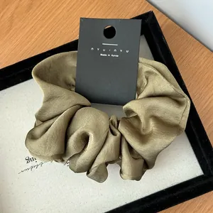Detailed view of large olive green satin scrunchie with elegant silk texture folds
