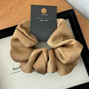 Close-up of champagne gold silk scrunchie with nyu nyu brand tag on velvet tray
