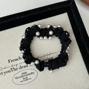 Detail shot of a black fabric scrunchie with elegant white pearl accents on jewelry tray