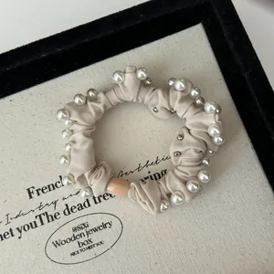 Detail of beige scrunchie with white faux pearls and metallic studs on a velvet tray
