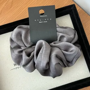 Detailed close-up of a charcoal gray satin scrunchie with refined pleated texture