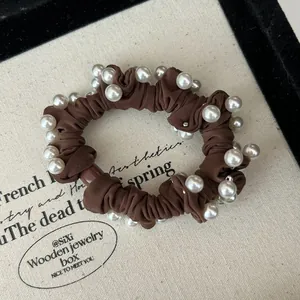 Detail of elegant brown elastic hair scrunchie with white faux pearls on a display tray