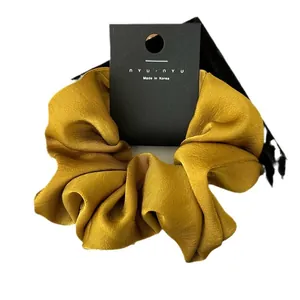 Elegant satin hair scrunchie in mustard yellow, displayed on minimalist black card