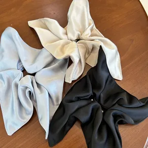 Detail of oversized satin bow scrunchies in silver, champagne, and black on a wooden table