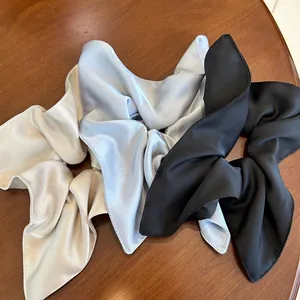 Close-up of three satin silk scrunchies with long ribbons in gold, blue, and black