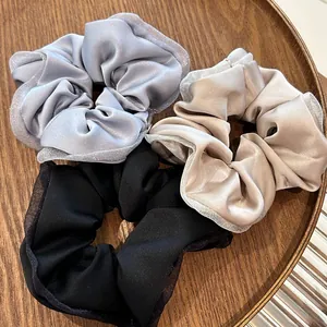 Detailed view of three satin scrunchies in grey, beige, and black on a wooden tray