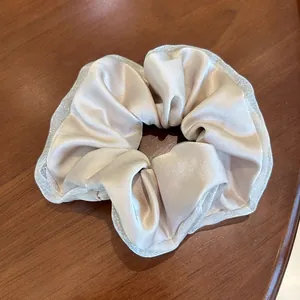 Detail shot of champagne satin hair scrunchie with sparkling mesh lace trim on wood