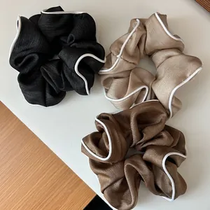 Lot de trois chouchous en satin avec liseré blanc en noir, champagne et marron