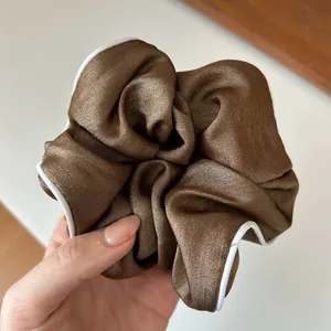 Gros plan sur un chouchou en satin marron café avec une bordure blanche contrastée