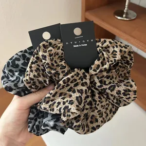Close-up of leopard print hair scrunchies in grey and brown fabric with brand labels