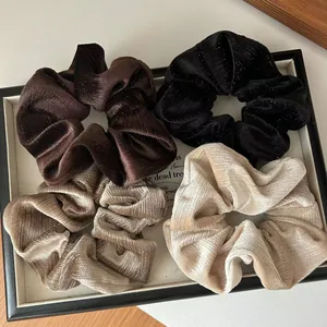 Détail de quatre chouchous en velours marron, noir, doré et gris avec texture pailletée