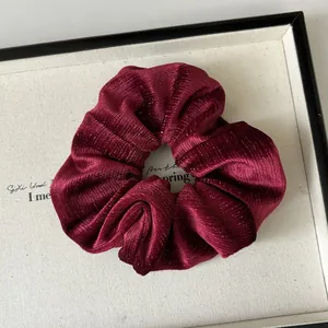 Gros plan sur un chouchou velours bordeaux avec paillettes métalliques et texture plissée