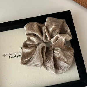 Gros plan sur un chouchou en velours doré champagne avec paillettes métalliques et plis doux