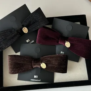 Detail of velvet bow hair clips in black, wine red, and brown with gold metal logo tags