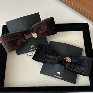 Close-up of velvet bow hair clips with gold logo plate and metallic thread texture