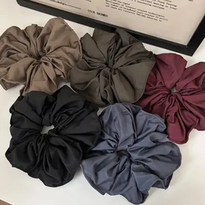Detail showing five large satin scrunchies in muted earth tones on a white background
