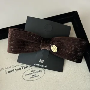 Macro detail of dark brown velvet bow hair clip with silver stripes and gold logo tag