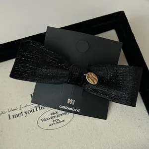Close-up of velvet bow hair clip with gold metal tag on black display card in a box