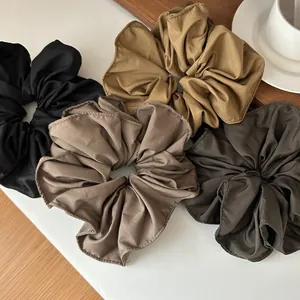 Detailed view of four large ruffled scrunchies in neutral earth tones on a white table