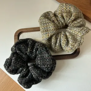 Detailed view of tweed knit scrunchies in brown and black on a rustic wooden tray