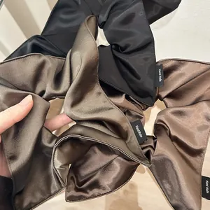 Detailed close-up of glossy satin scrunchies with handmade woven labels in earthy tones