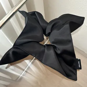 Detail of a large black satin scrunchie with handmade label and glossy silk texture
