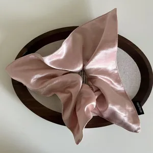Elegant pink satin bow hair scrunchie with handmade label on a decorative tray