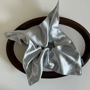 Macro view of silky silver-grey satin scrunchie with a Hand Made woven label on wood